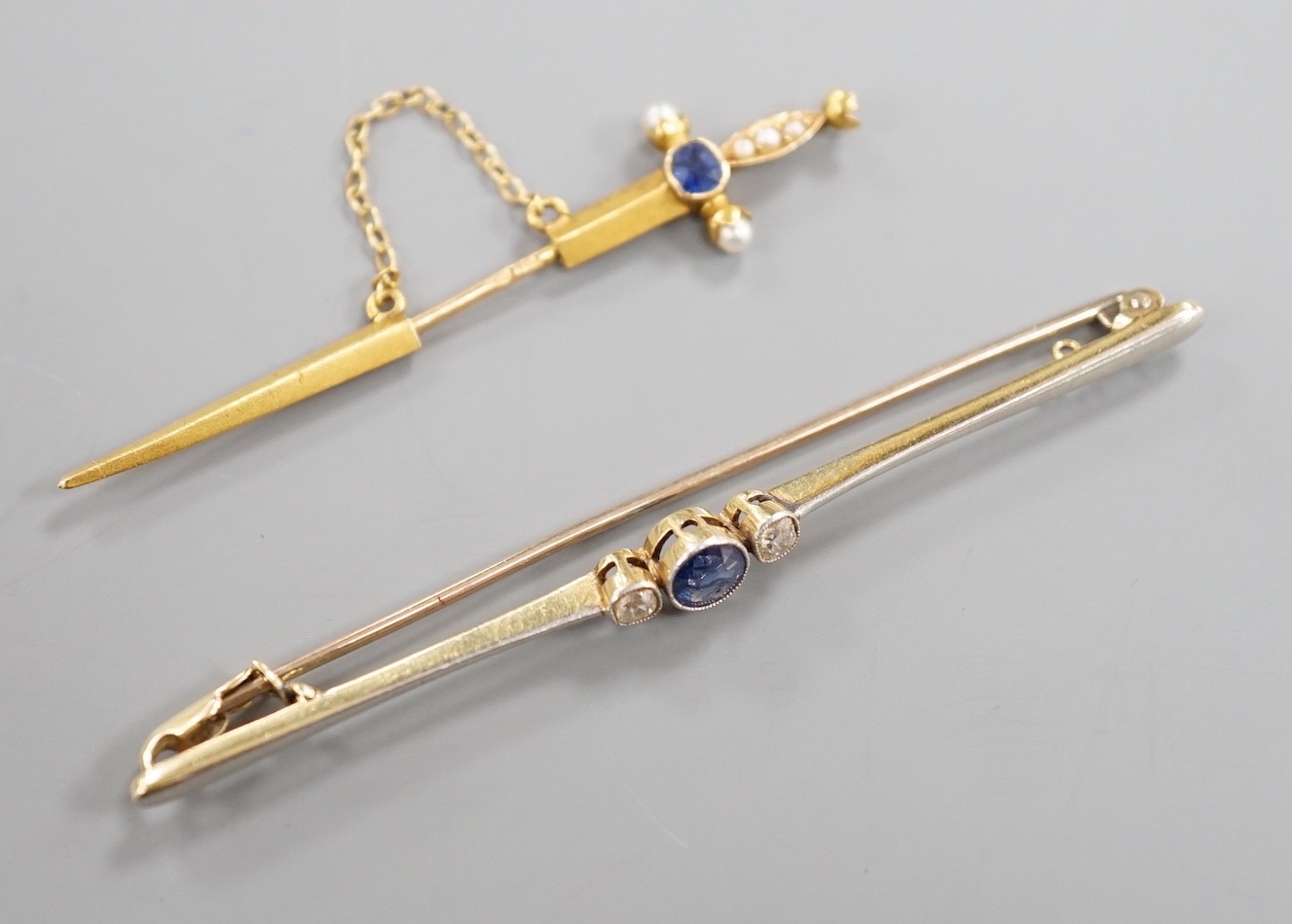 An early 20th French yellow metal (18ct poincon mark), sapphire and seed pearl set jabot pin, modelled a sword, 49mm, gross 1.3 grams and an Edwardian 15ct, sapphire and diamond set bar brooch, gross weight 3.2 grams.